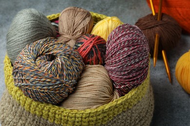 Photo of Soft woolen yarns and knitting needles on grey table, closeup