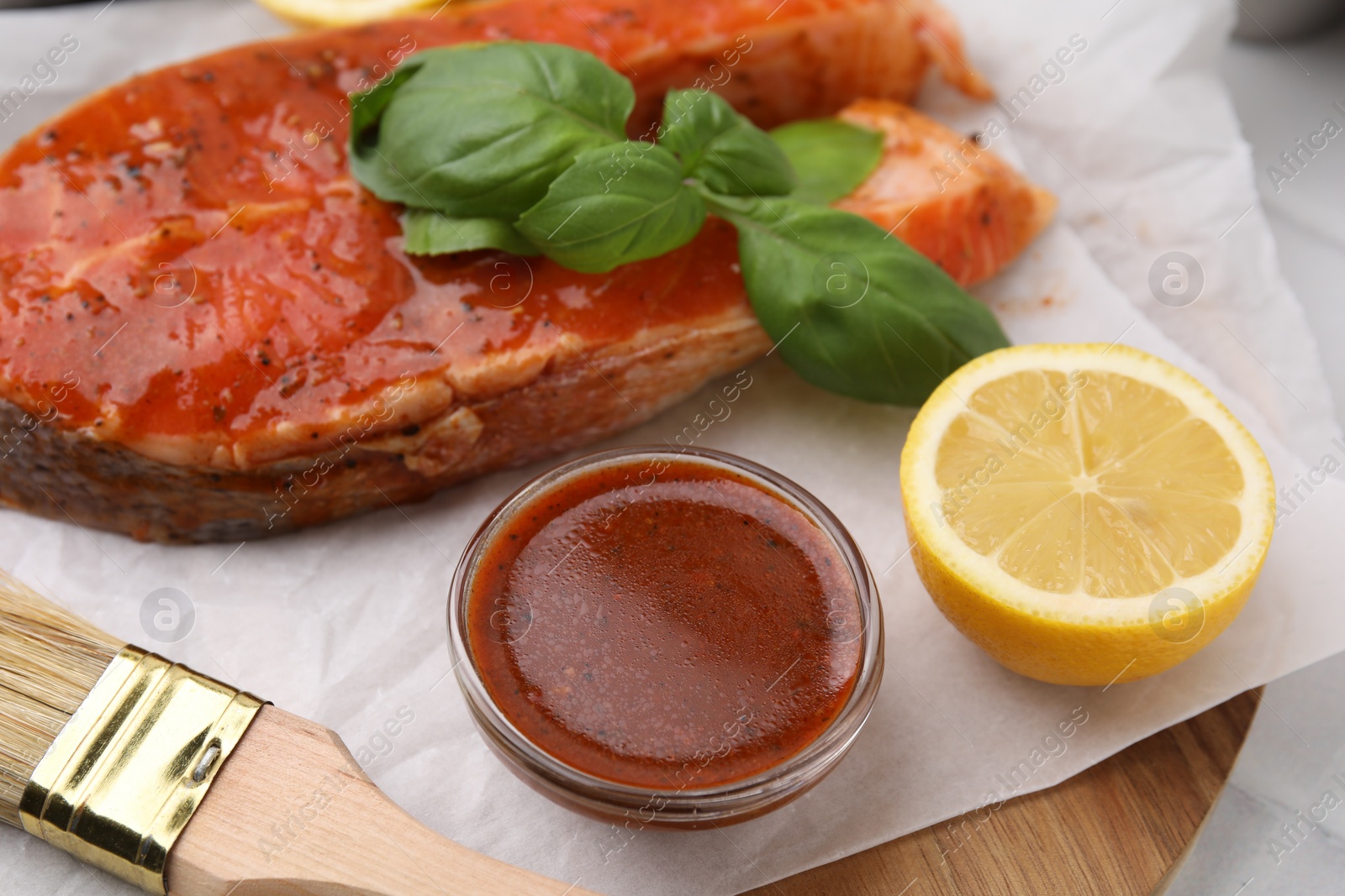 Photo of Fresh marinade, fish, lemon, brush and basil on table, closeup