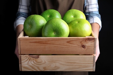Photo of Woman holding wooden crate with sweetie fruits on black background, closeup