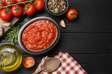 Photo of Homemade tomato sauce in bowl, spoon and fresh ingredients on black wooden table, flat lay. Space for text