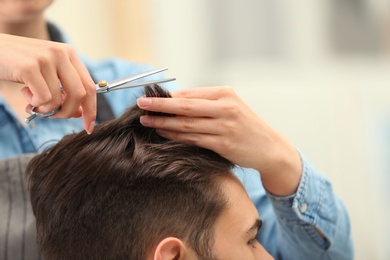 Photo of Barber making stylish haircut with professional scissors in beauty salon, closeup