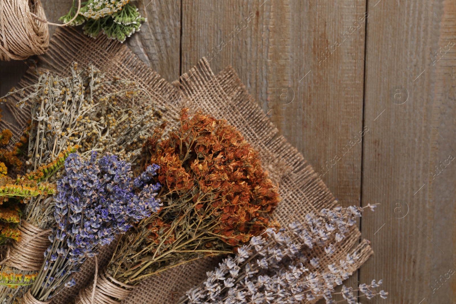Photo of Different dry herbs and burlap fabric on wooden table, flat lay. Space for text