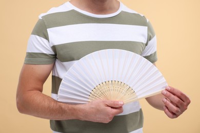 Photo of Man holding hand fan on beige background, closeup