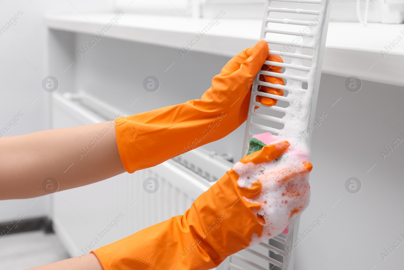 Photo of Woman washing radiator grill with sponge and detergent indoors, closeup