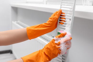 Photo of Woman washing radiator grill with sponge and detergent indoors, closeup