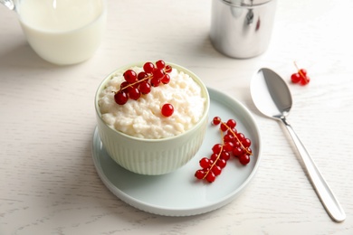 Photo of Creamy rice pudding with red currant in bowl served on white wooden table