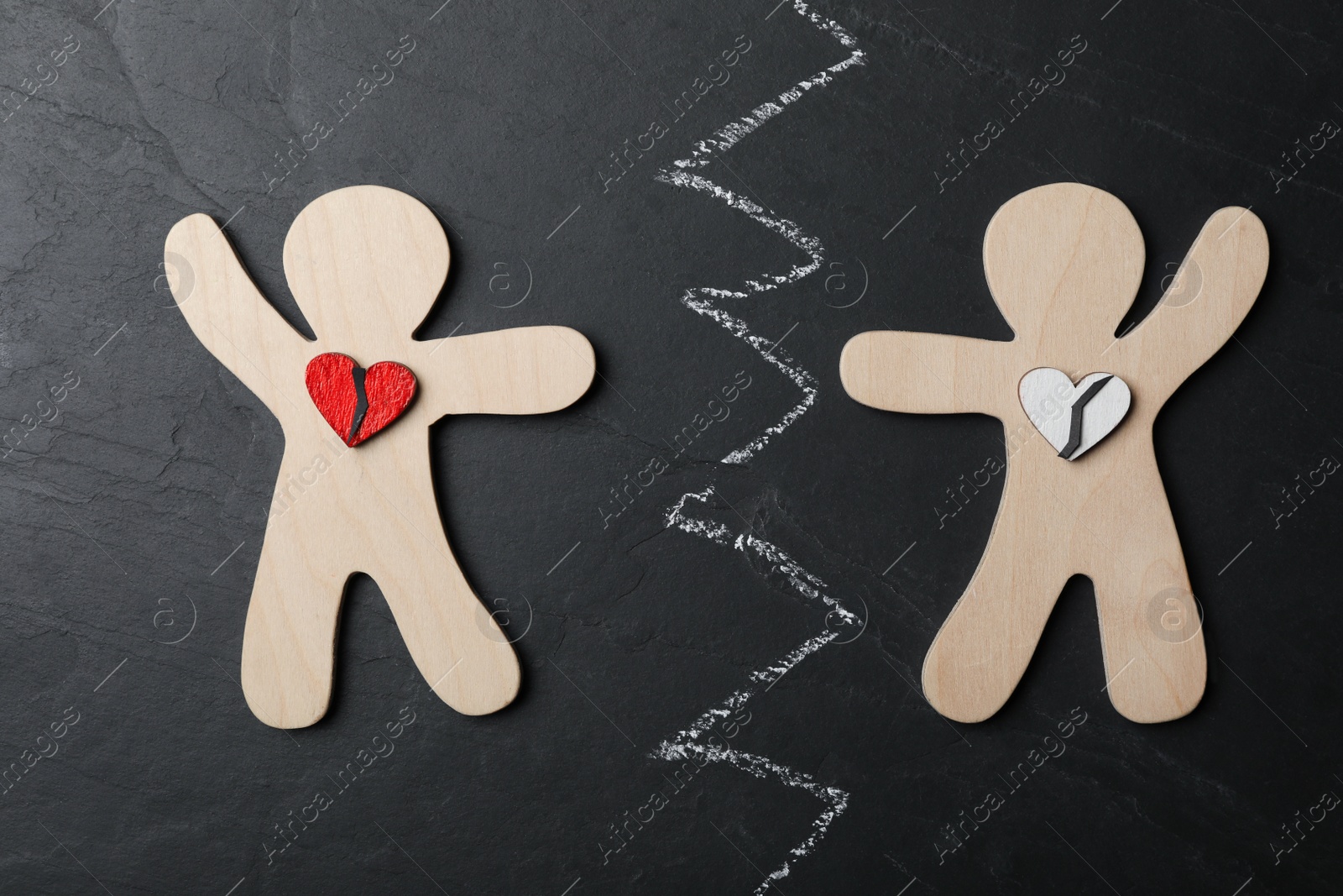 Photo of Human figures with broken hearts divided by chalk line on black stone background, flat lay. Relationship problems concept