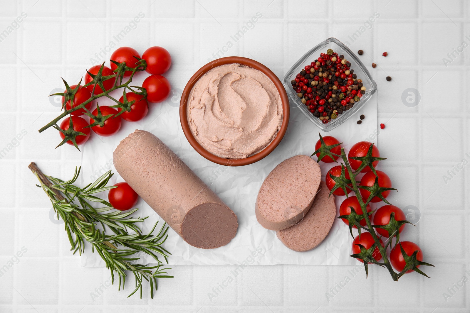 Photo of Delicious liver sausage, paste and other products on white tiled table, flat lay