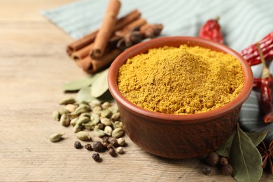 Photo of Curry powder in bowl and other spices on wooden table, closeup. Space for text