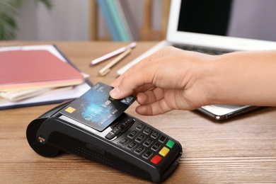 Woman using terminal for contactless payment with credit card at table