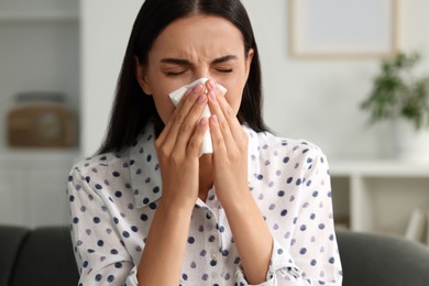 Photo of Suffering from allergy. Young woman blowing her nose in tissue at home
