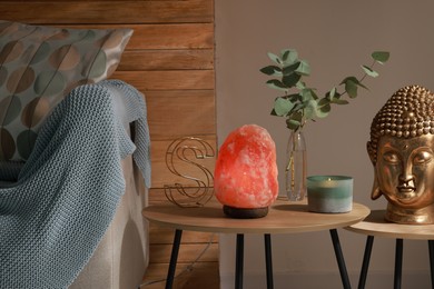 Photo of Beautiful Himalayan salt lamp, golden Buddha sculpture and decor on wooden tables in living room