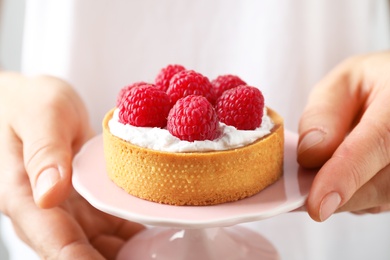 Photo of Woman holding cake stand with raspberry tart, closeup. Delicious pastries