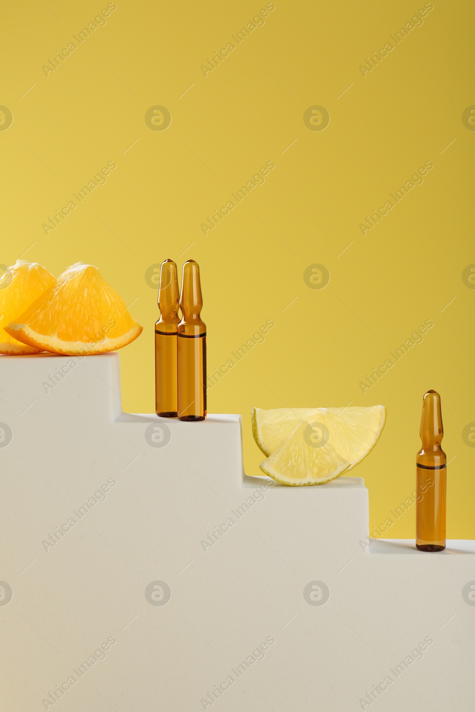 Photo of Stylish presentation of skincare ampoules with vitamin C and citrus slices on decorative stairs against yellow background, closeup. Space for text