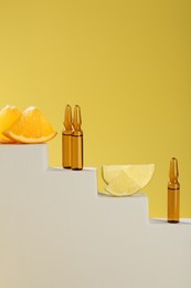 Stylish presentation of skincare ampoules with vitamin C and citrus slices on decorative stairs against yellow background, closeup. Space for text