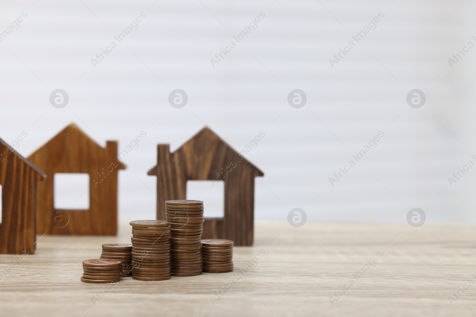 Photo of House models and stacked coins on wooden table, space for text