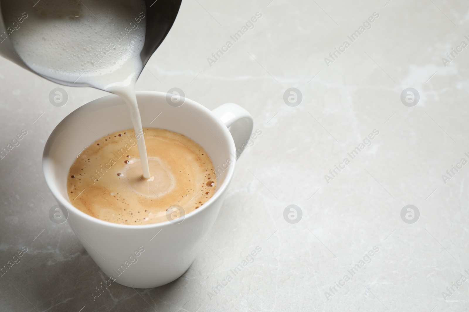 Photo of Pouring milk into cup of coffee on grey table, closeup. Space for text