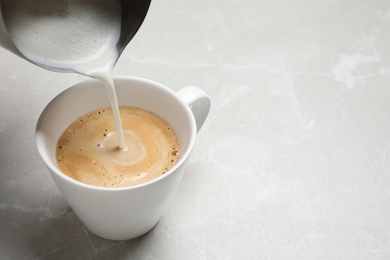 Photo of Pouring milk into cup of coffee on grey table, closeup. Space for text