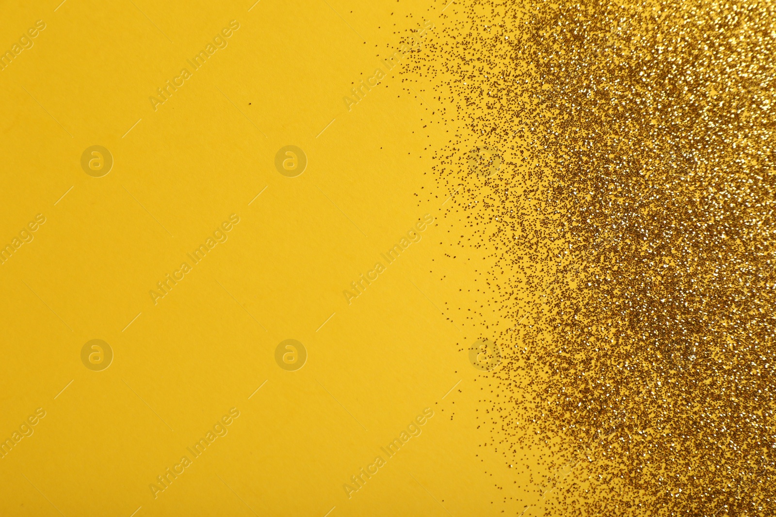 Photo of Shiny golden glitter on yellow background, top view. Space for text