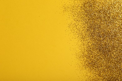 Photo of Shiny golden glitter on yellow background, top view. Space for text