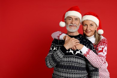 Photo of Senior couple in Christmas sweaters and Santa hats on red background. Space for text