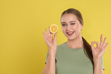 Young woman with cut lemon on yellow background, space for text. Vitamin rich food