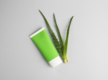 Tube of toothpaste and fresh aloe on light grey background, flat lay