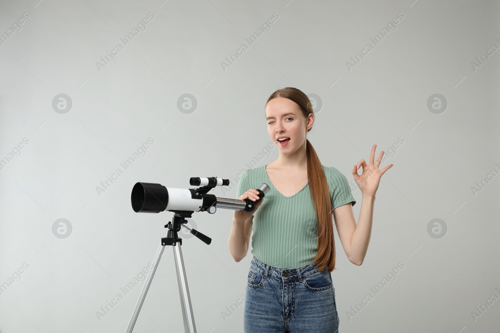 Photo of Excited astronomer with telescope showing OK gesture on grey background