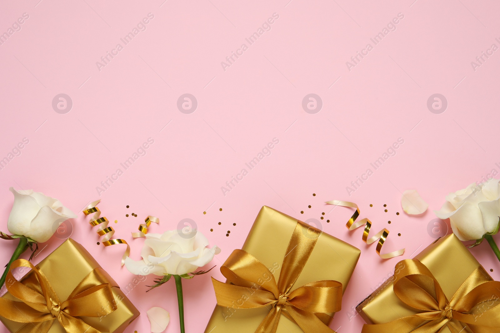 Photo of Golden gift boxes, white roses, confetti and streamers on pink background, flat lay. Space for text