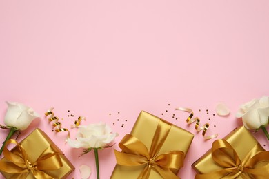 Photo of Golden gift boxes, white roses, confetti and streamers on pink background, flat lay. Space for text