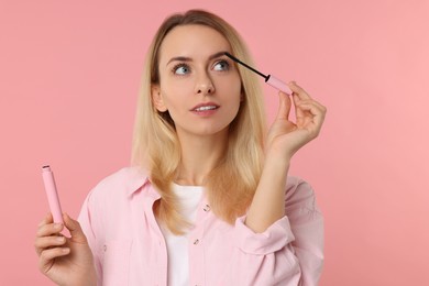 Beautiful woman applying mascara on pink background