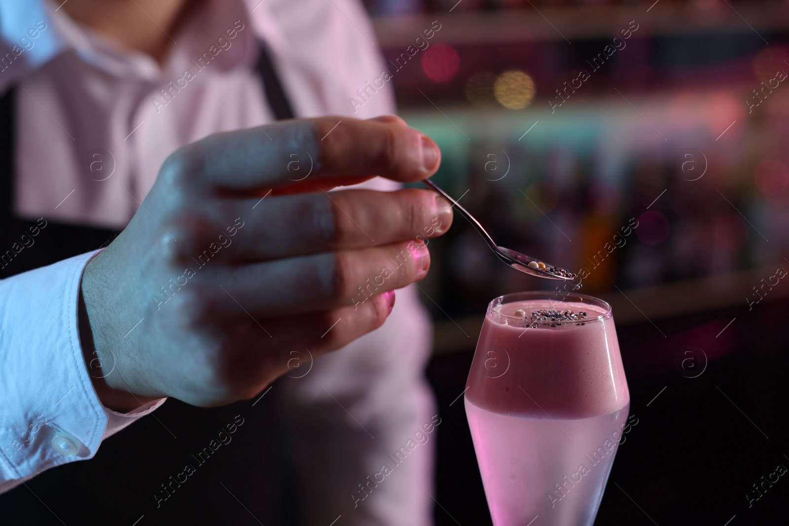 Photo of Bartender decorating fresh alcoholic cocktail with sprinkles on blurred background, closeup