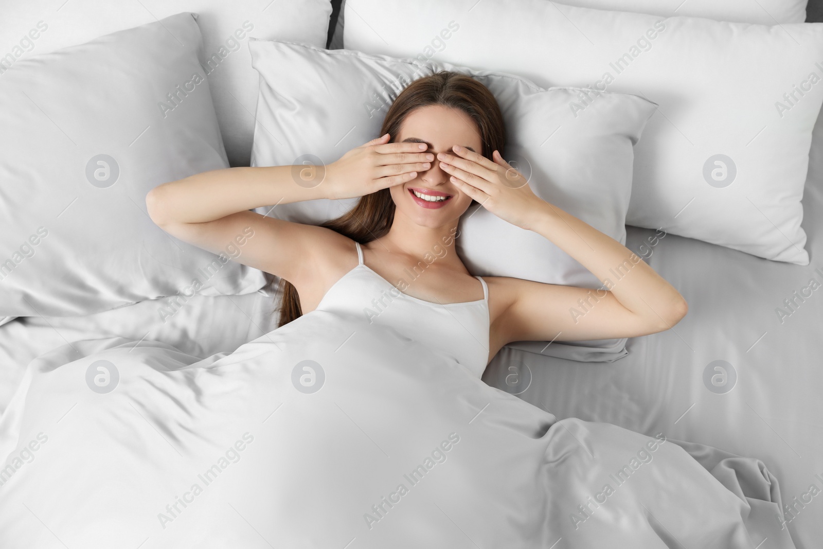 Photo of Young woman awaking in comfortable bed with silky linens, above view