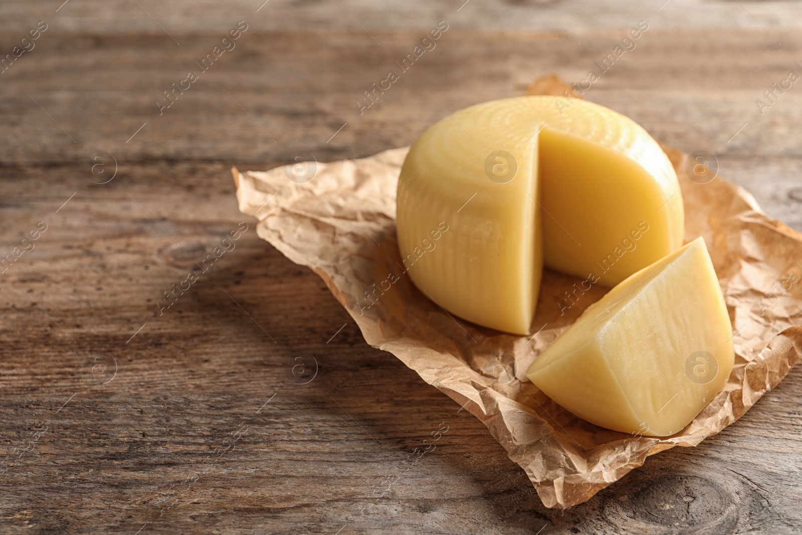 Photo of Parchment paper with cut wheel of delicious cheese on wooden table. Space for text