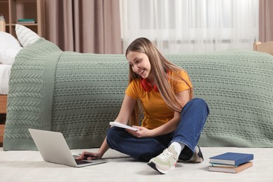 Photo of Online learning. Teenage girl with notepad typing on laptop near bed at home