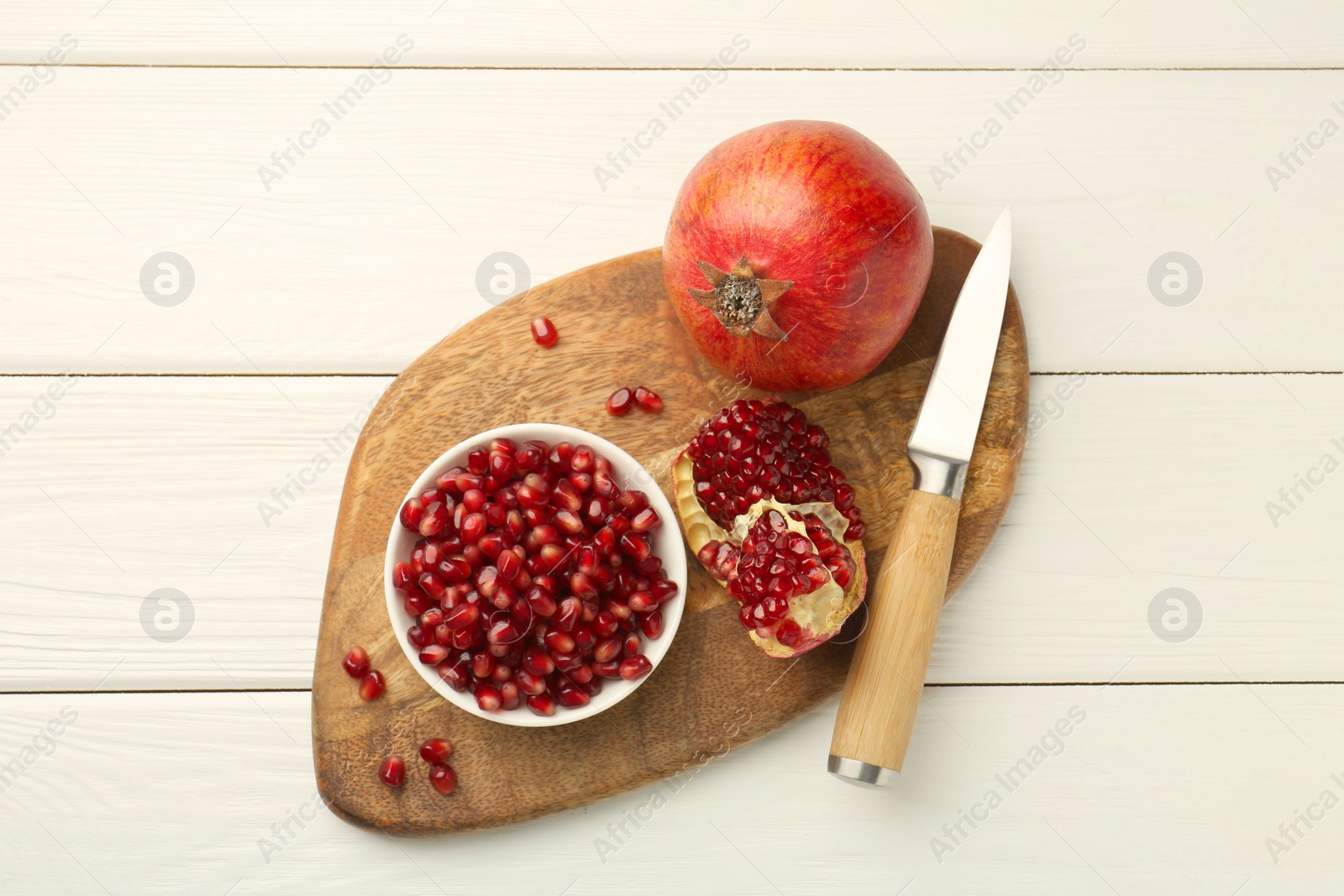 Photo of Ripe juicy pomegranate with grains and knife on white wooden table, top view