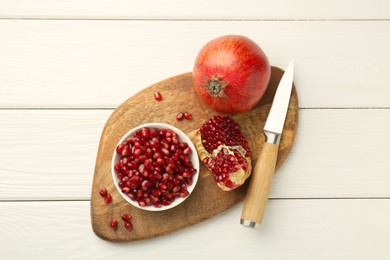 Photo of Ripe juicy pomegranate with grains and knife on white wooden table, top view