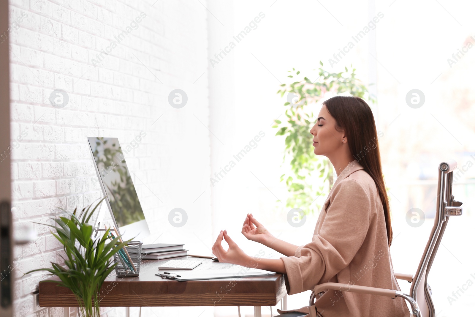 Photo of Young businesswoman meditating at workplace. Zen concept