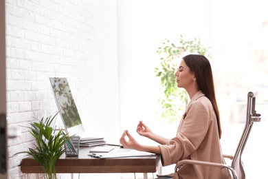 Photo of Young businesswoman meditating at workplace. Zen concept