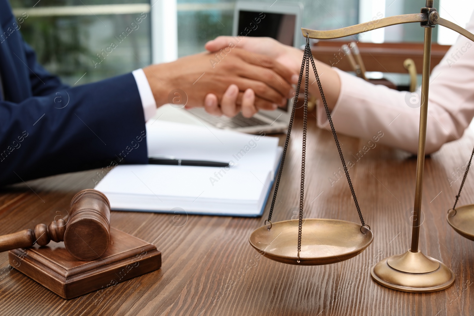 Photo of Gavel, scales and blurred lawyer handshaking with client on background