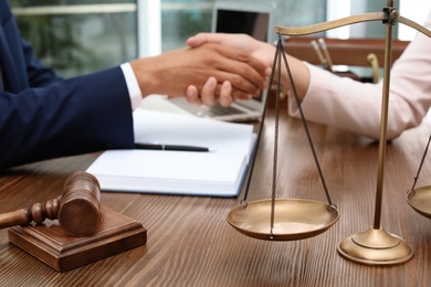 Gavel, scales and blurred lawyer handshaking with client on background