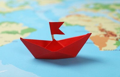 Photo of Red paper boat with flag on world map