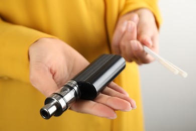 Photo of Woman with cigarettes and vaping device on light background, closeup. Smoking alternative