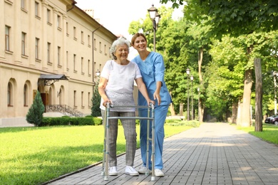 Photo of Happy nurse assisting elderly woman with walking frame at park