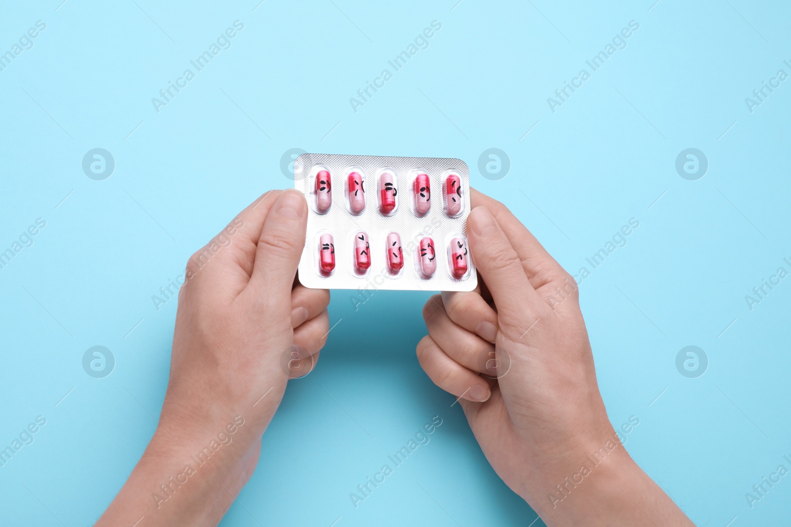 Photo of Woman holding antidepressants with different emoticons on light blue background, top view