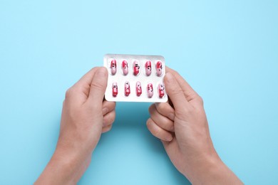 Woman holding antidepressants with different emoticons on light blue background, top view