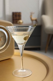 Photo of Martini cocktail with olive and retro radio receiver on table in room. Relax at home