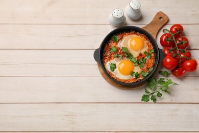 Photo of Delicious shakshuka in frying pan on light wooden table, flat lay. Space for text