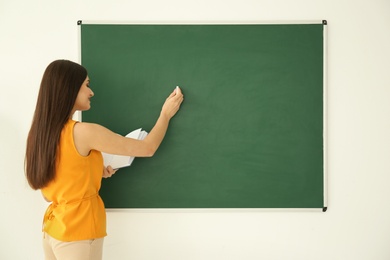 Photo of Young female teacher writing on blackboard in classroom