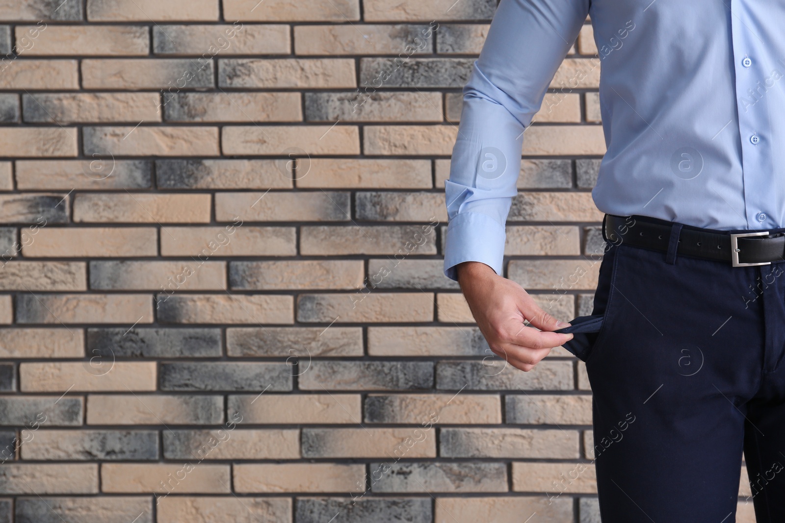 Photo of Businessman showing empty pocket near brick wall, closeup. Space for text